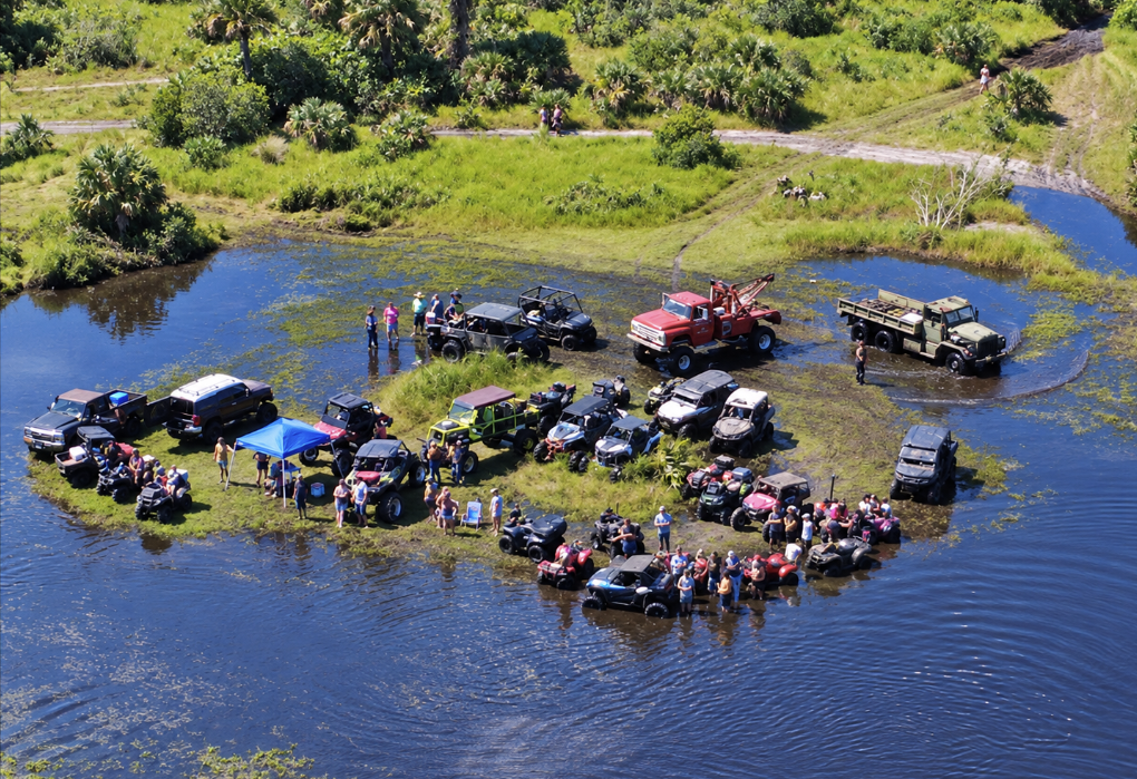 Off-road vehicles and people gathered on a small dry area surrounded by water